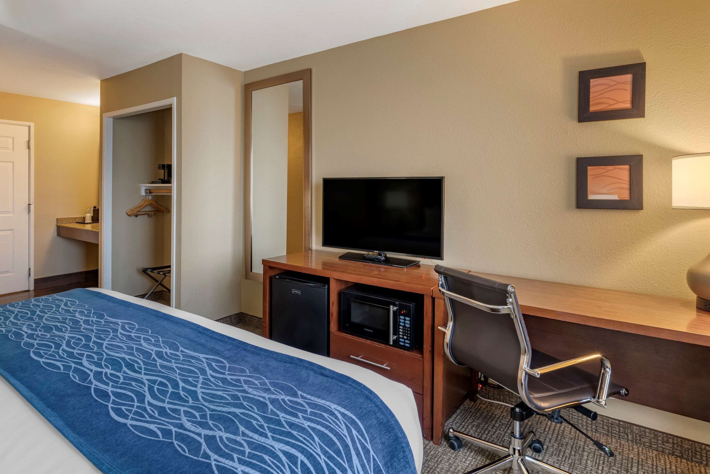 A hotel room with a bed, a desk with a television, a microwave, and a chair.