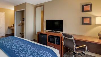 Una habitación de hotel con una cama, un escritorio con televisor, un microondas y una silla.