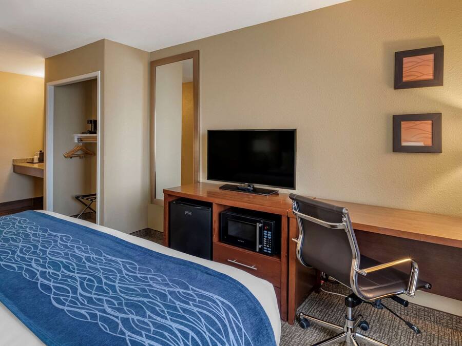 Una habitación de hotel con una cama, un escritorio con televisor, un microondas y una silla.