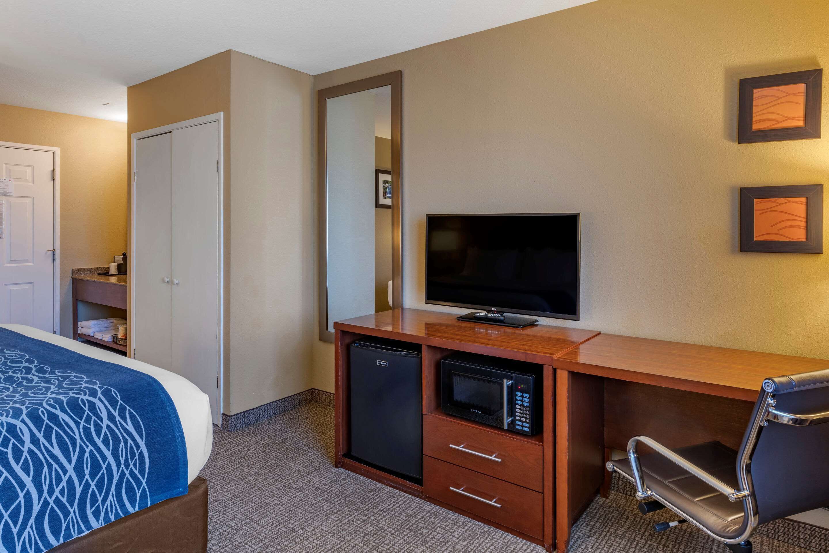 A hotel room with a bed, a desk with a television, a microwave, and a refrigerator.