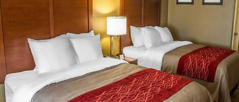 A hotel room with two beds, a wooden headboard, a nightstand with a lamp, and two framed pictures on the wall.