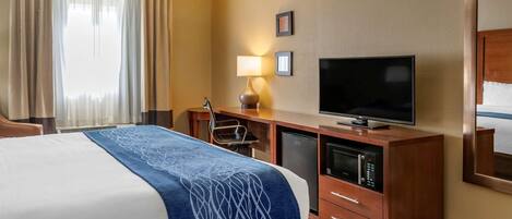Ein Hotelzimmer mit einem Bett, einem Schreibtisch mit Fernseher, einer Lampe und einer Minibar.