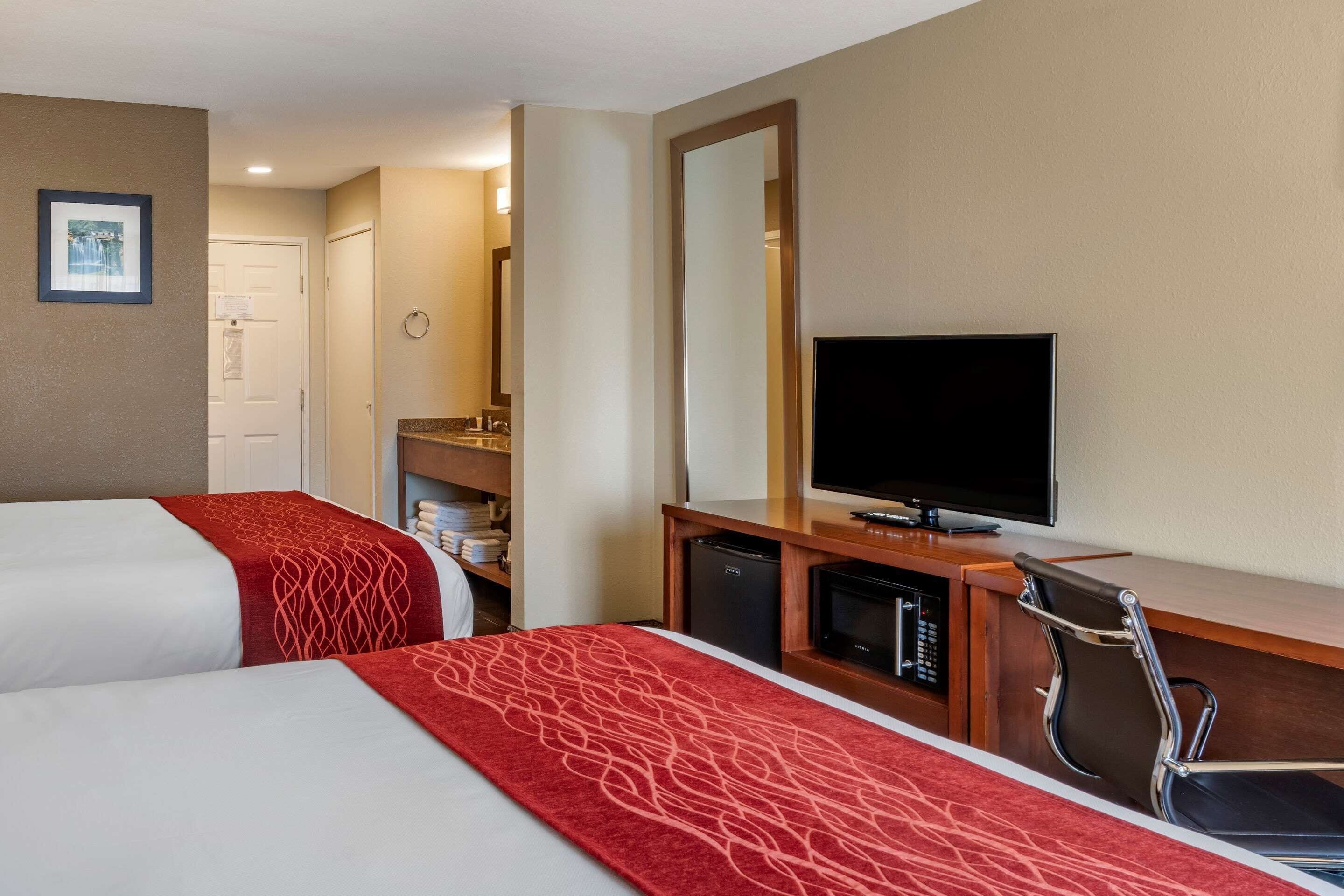 A hotel room with two beds, a television, a desk with a chair, and a mirror.