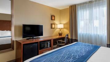 A hotel room with a bed, TV, microwave, and a desk with a lamp.