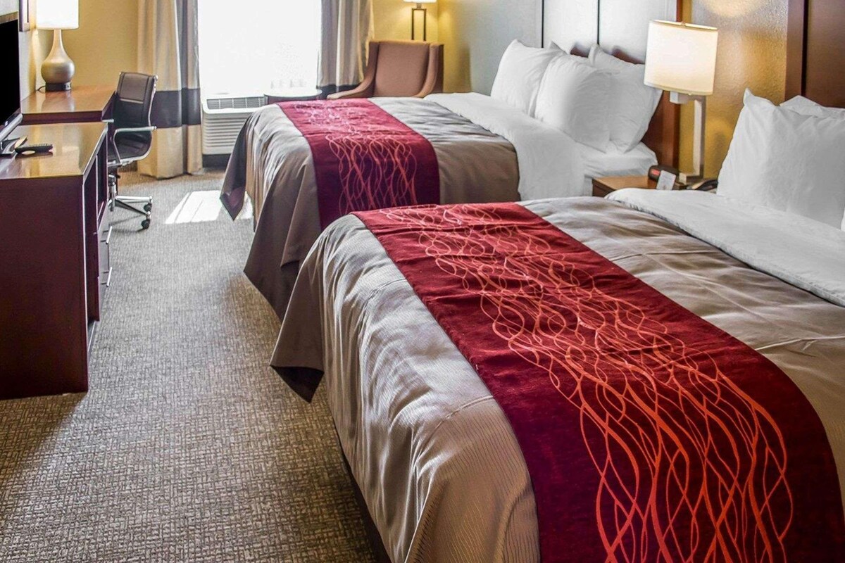 Una habitación de hotel con dos camas, un escritorio, una silla y una lámpara.