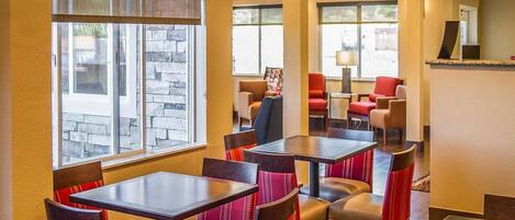 A restaurant with multiple tables and chairs, large windows, and a stone wall.