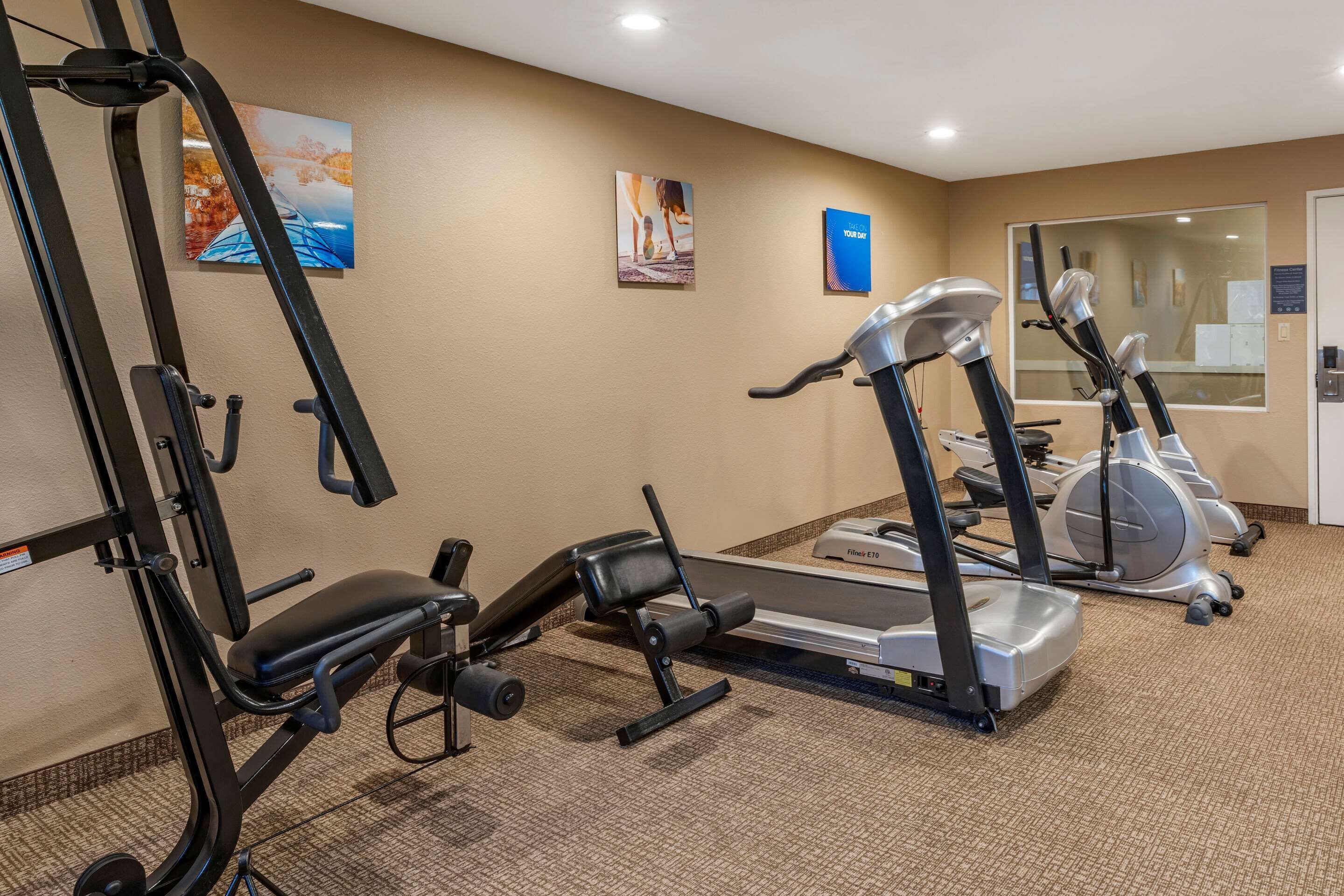 A fitness center with cardio machines, weight machines, and a wall-mounted TV.