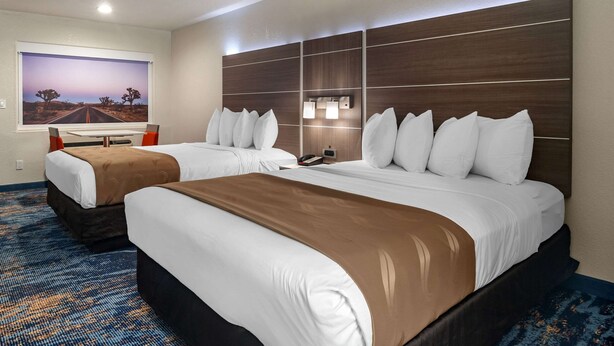 A hotel room with two beds, a large window with a desert landscape view, a desk with a chair, and a wall-mounted light fixture. - Quality Inn Blythe I-10 (Blythe)