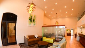 A spacious lobby with a sofa, armchairs, a coffee table, and a patterned rug. There are ceiling lights and a large window with curtains. - Quality Inn Blythe I-10 (Blythe)