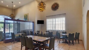 A dining area with multiple tables and chairs, a television mounted on the wall, and a large window with curtains. - Quality Inn Blythe I-10 (Blythe)