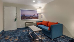 A hotel room with a blue sofa, an orange pillow, a small table, a framed picture on the wall, and a ceiling light. - Quality Inn Blythe I-10 (Blythe)