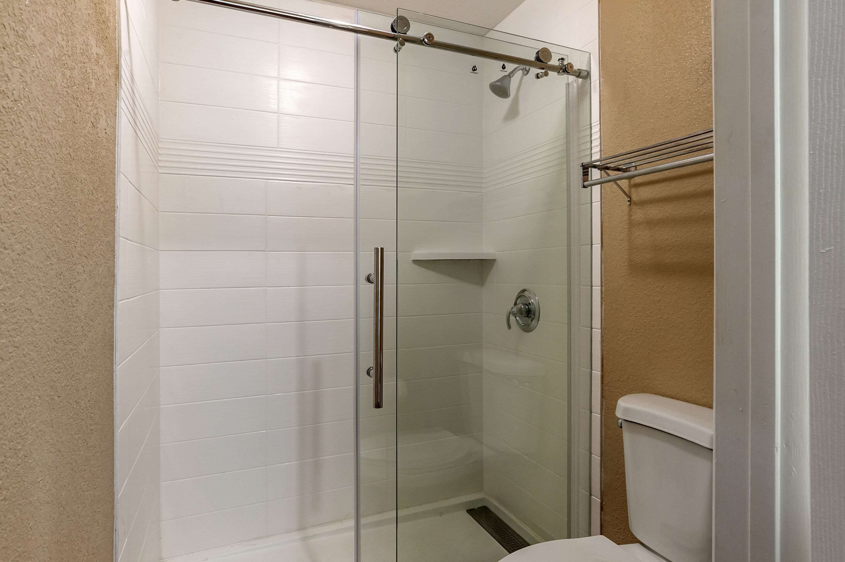 A glass-enclosed shower stall with a white toilet and a towel rack.
