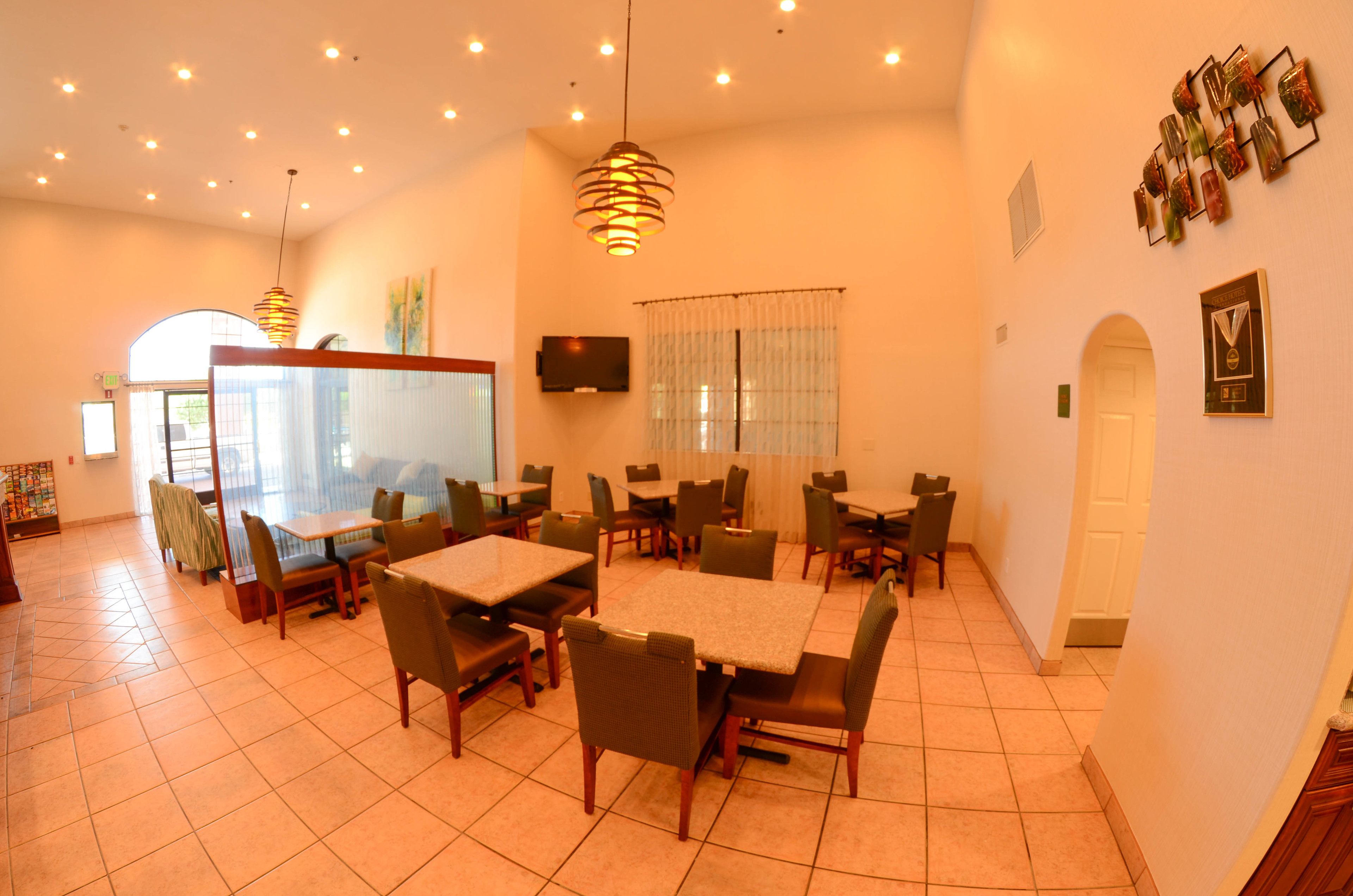 A dining area with tables and chairs, a television on the wall, and a large window with curtains.