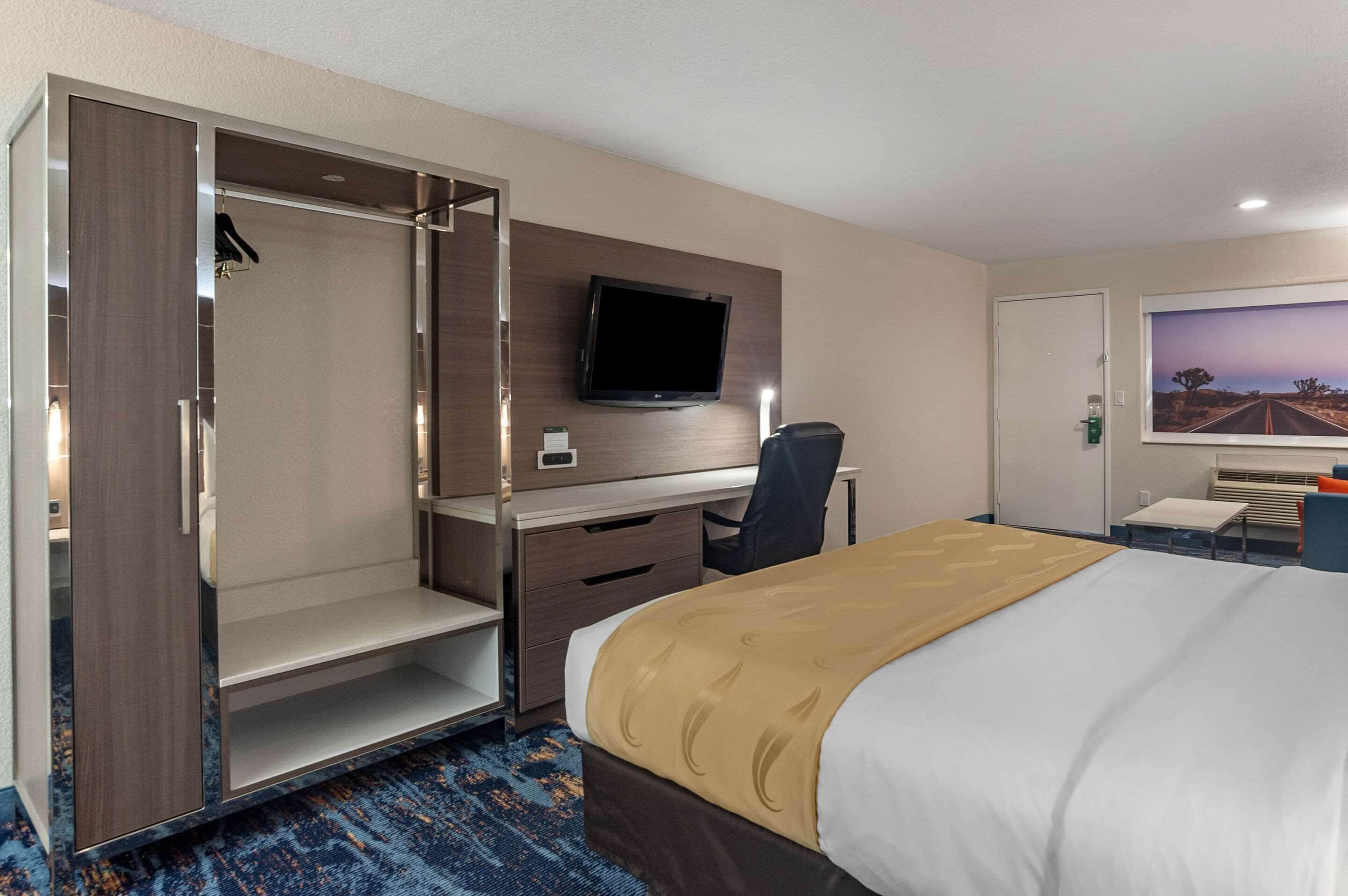 Een hotelkamer met een bed, een bureau met stoel, een televisie, een kledingkast en een schilderij aan de muur.
