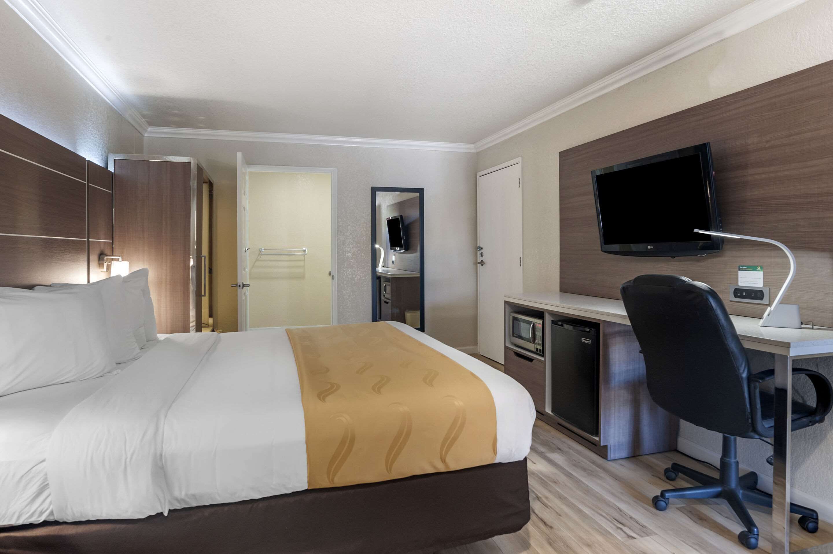 A hotel room with a bed, a desk with a computer, a TV, and a mirror.
