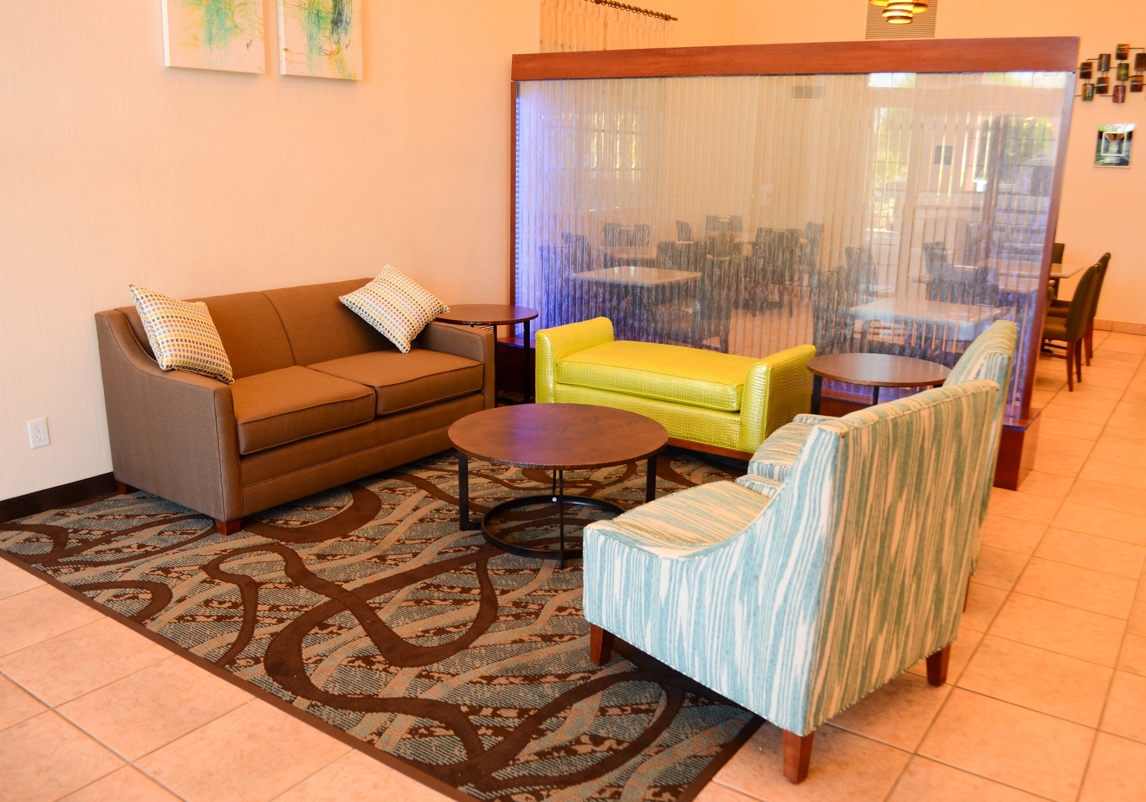 A living room with a brown sofa, a yellow armchair, a striped armchair, a round coffee table, and a patterned rug.