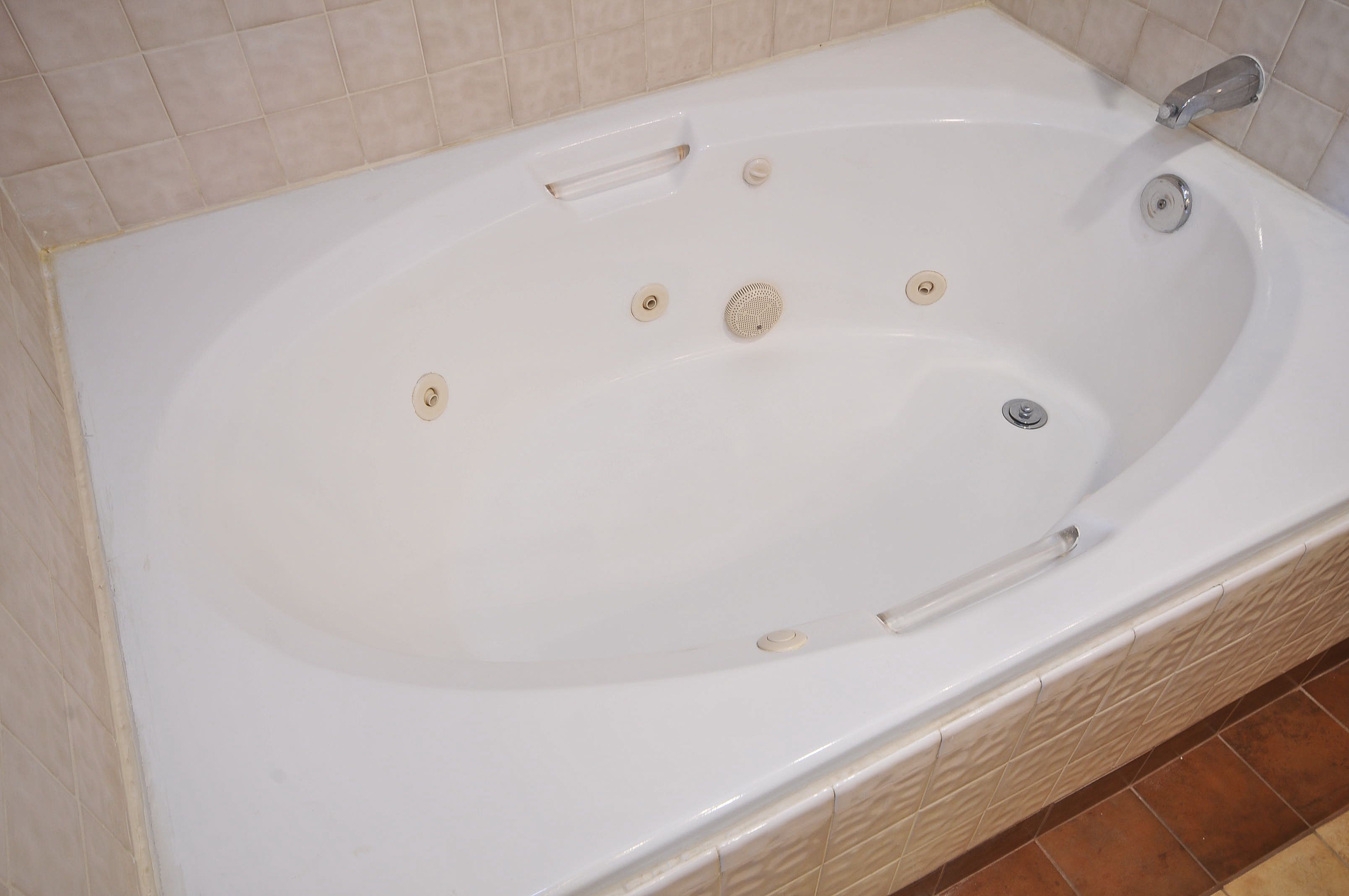 Eine weiße Badewanne mit integriertem Sitz, einer Handbrause und einem Ablaufsieb.