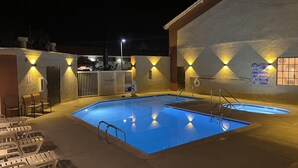 A swimming pool with lounge chairs and a bar area, surrounded by walls with illuminated signs.