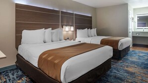 A hotel room with two beds, a large wooden headboard, a nightstand, and a bathroom with a mirror.