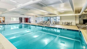 An indoor swimming pool with clear water, lounge chairs, and a stone fireplace. - Best Western Springfield Hotel (Springfield)