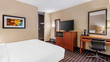Une chambre d’hôtel avec un lit, un bureau équipé d’un ordinateur, une télévision, un miroir et un tableau encadré au mur.