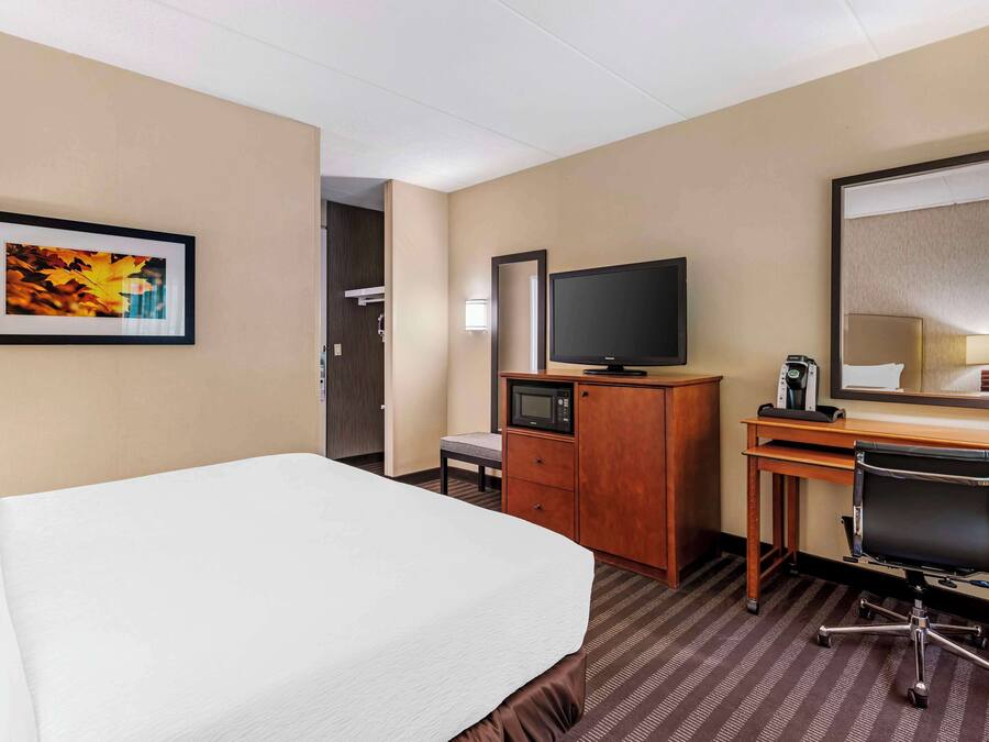 Une chambre d’hôtel avec un lit, un bureau équipé d’un ordinateur, une télévision, un miroir et un tableau encadré au mur.