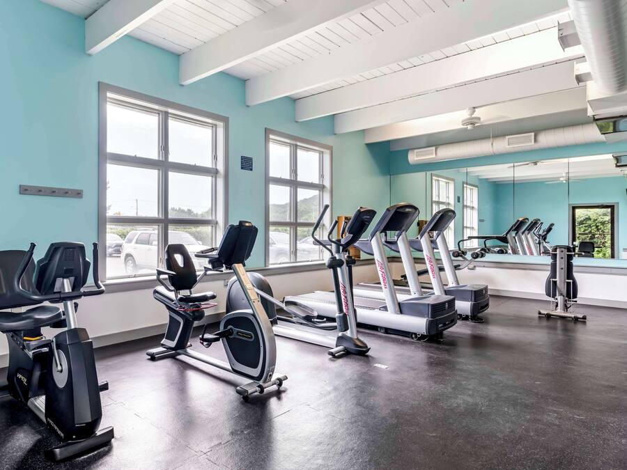 Uma academia com equipamentos de exercício, janelas amplas e vista para o exterior.