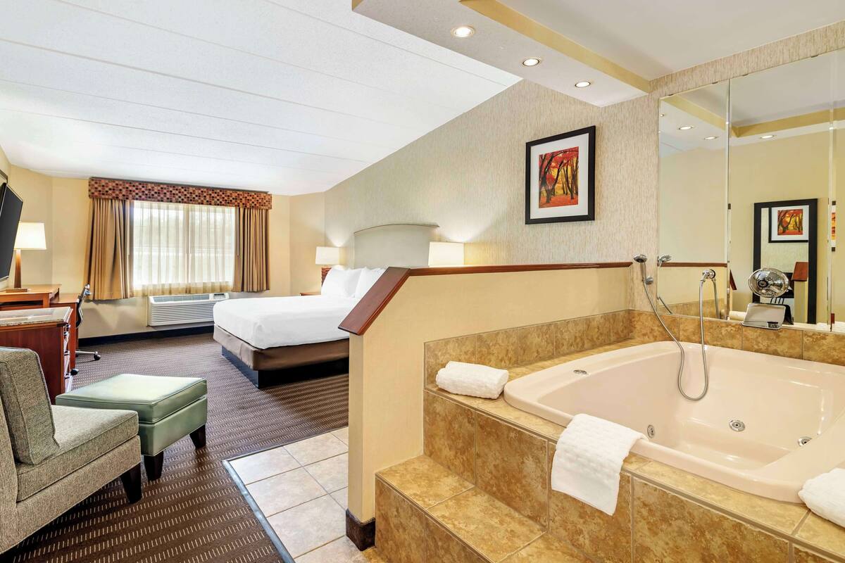 A hotel room with a bed, a sitting area, a bathroom with a bathtub, and a large mirror.