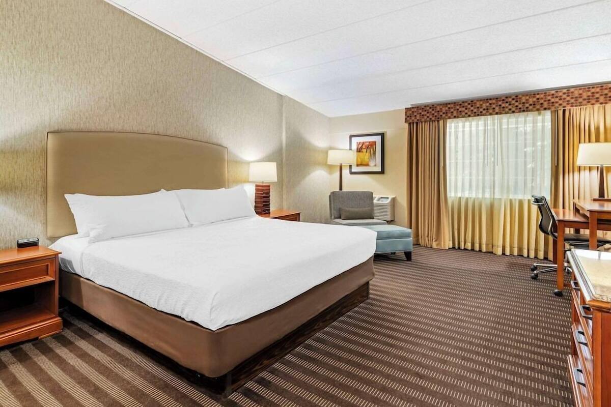 A hotel room with a large bed, a desk, a chair, a lamp, and a window with curtains.