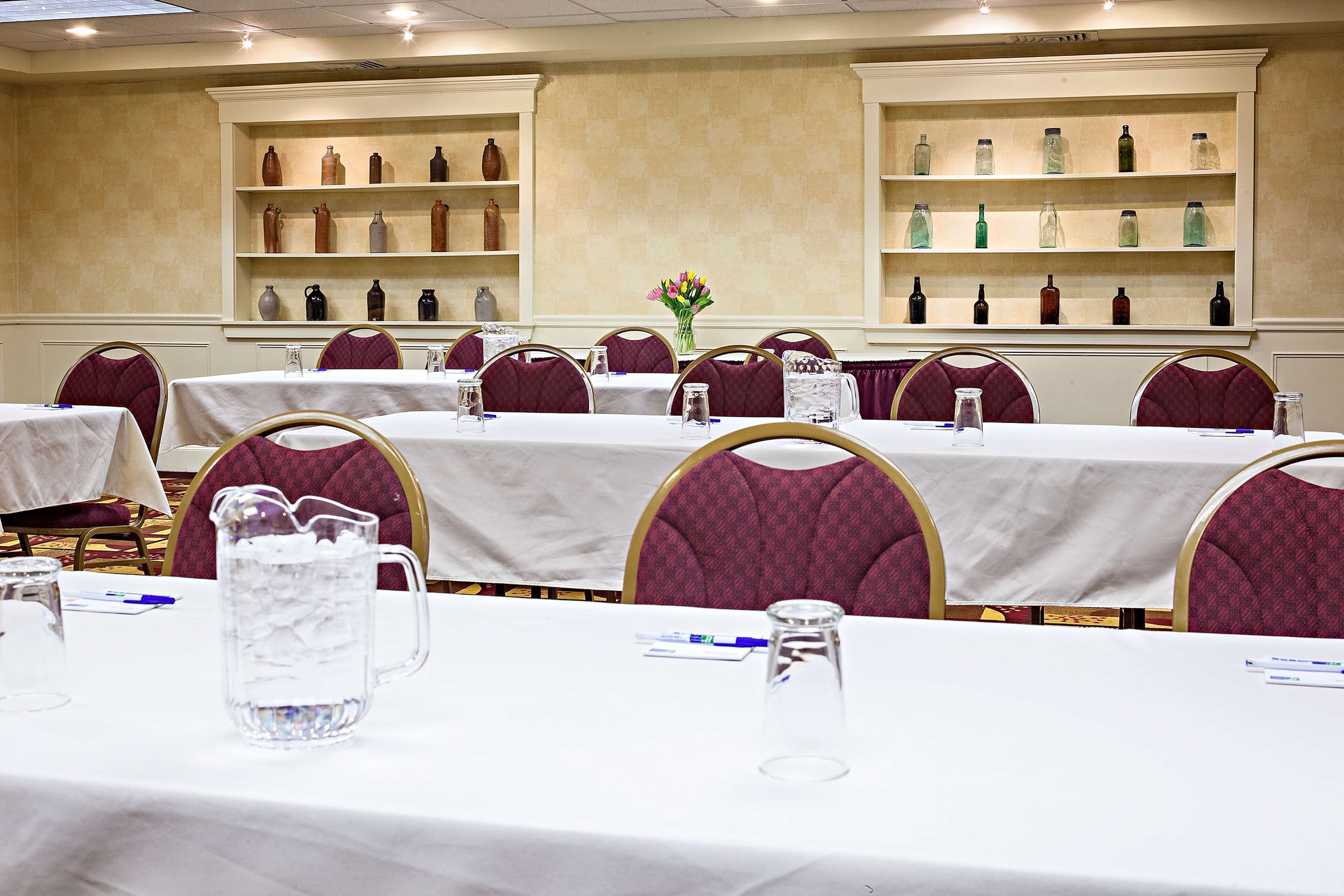 A conference room with tables set for meetings, equipped with water pitchers and glasses, and surrounded by shelves with decorative vases.