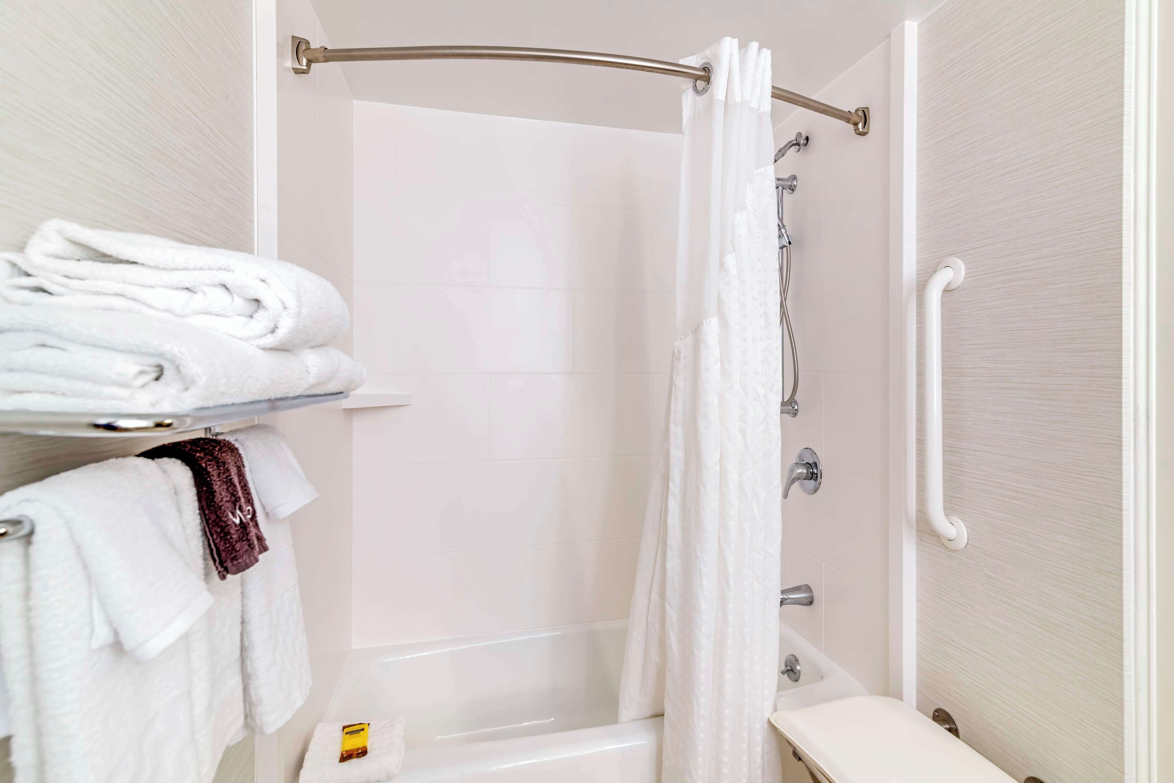 A bathroom with a shower, a toilet, and a sink. There are towels on a shelf and a shower curtain.
