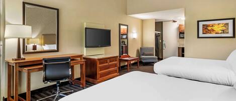 A hotel room with a bed, desk, chair, TV, and a small seating area.
