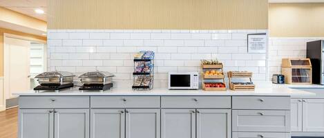 Une cuisine moderne avec un crédence en carreaux blancs, un four à micro-ondes encastré et une variété d’aliments disposés sur le plan de travail.