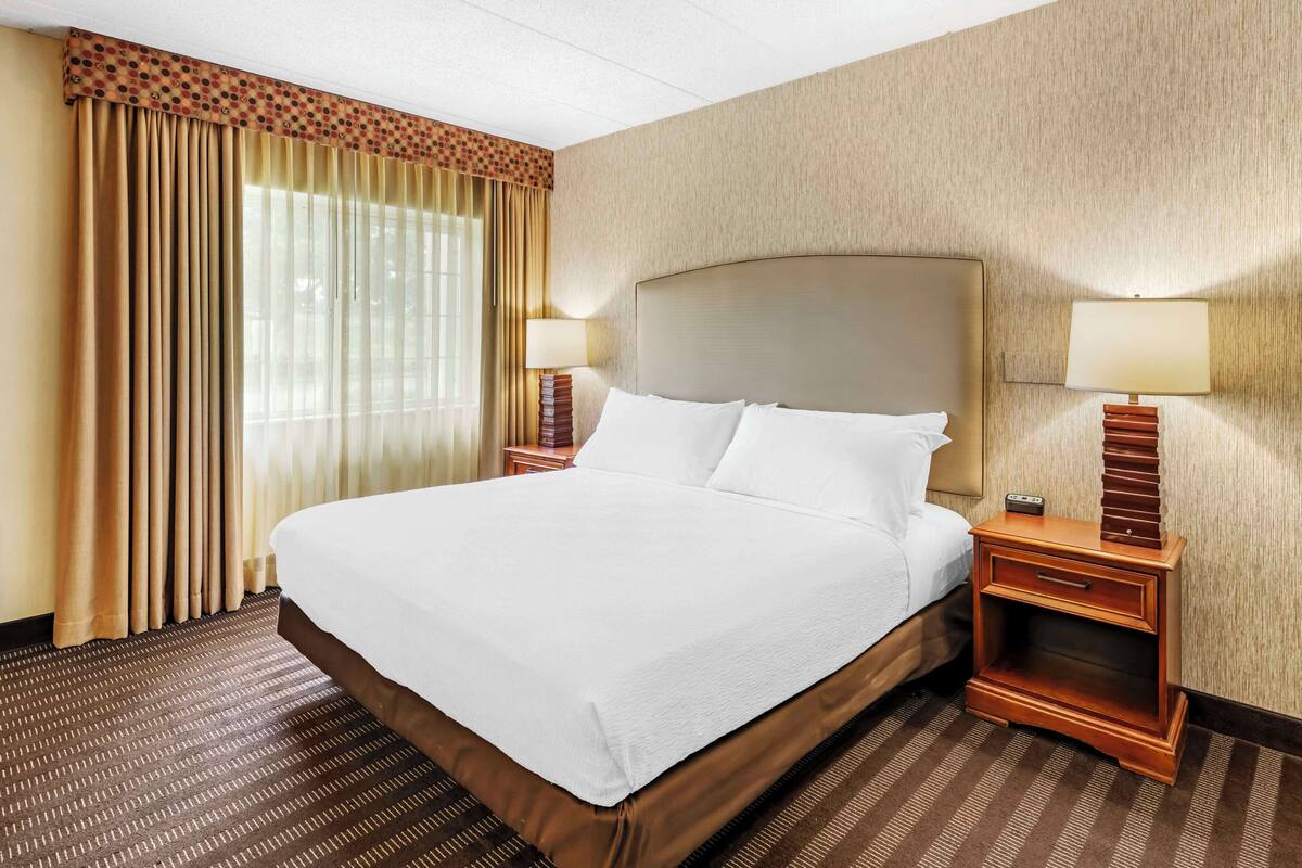A hotel room with a large bed, two bedside tables, a lamp, and a window with curtains.