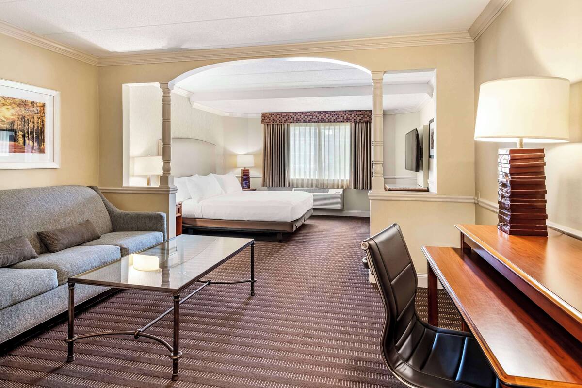 A hotel room with a bed, a sofa, a coffee table, a desk, and a TV.
