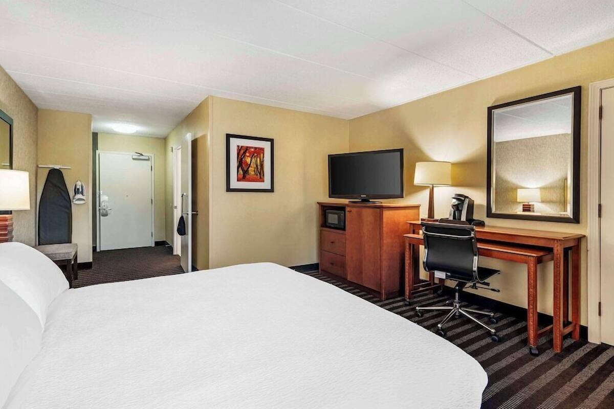 A hotel room with a large bed, a desk with a computer, a TV, and a mirror.