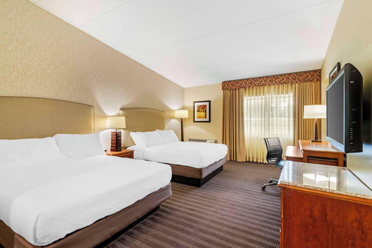 A hotel room with two beds, a desk, a television, and a window with curtains.