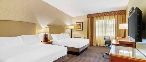 A hotel room with two beds, a desk, a television, and a window with curtains.