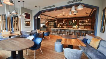 A modern bar area with wooden tables, blue chairs, and a brick wall backdrop.