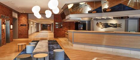 A modern hotel lobby with a reception desk, seating area, and a check-out counter.