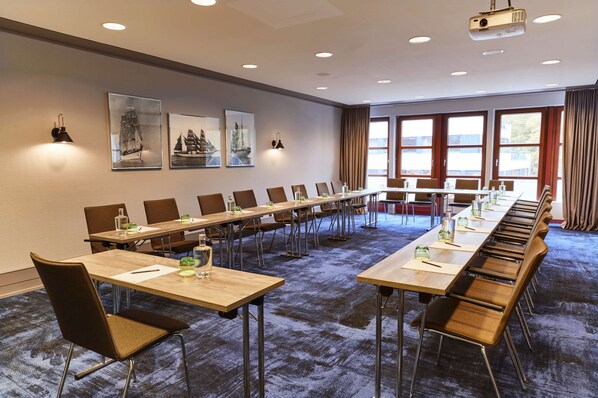 Une salle de conférence équipée de longues tables, de chaises et d’un projecteur.