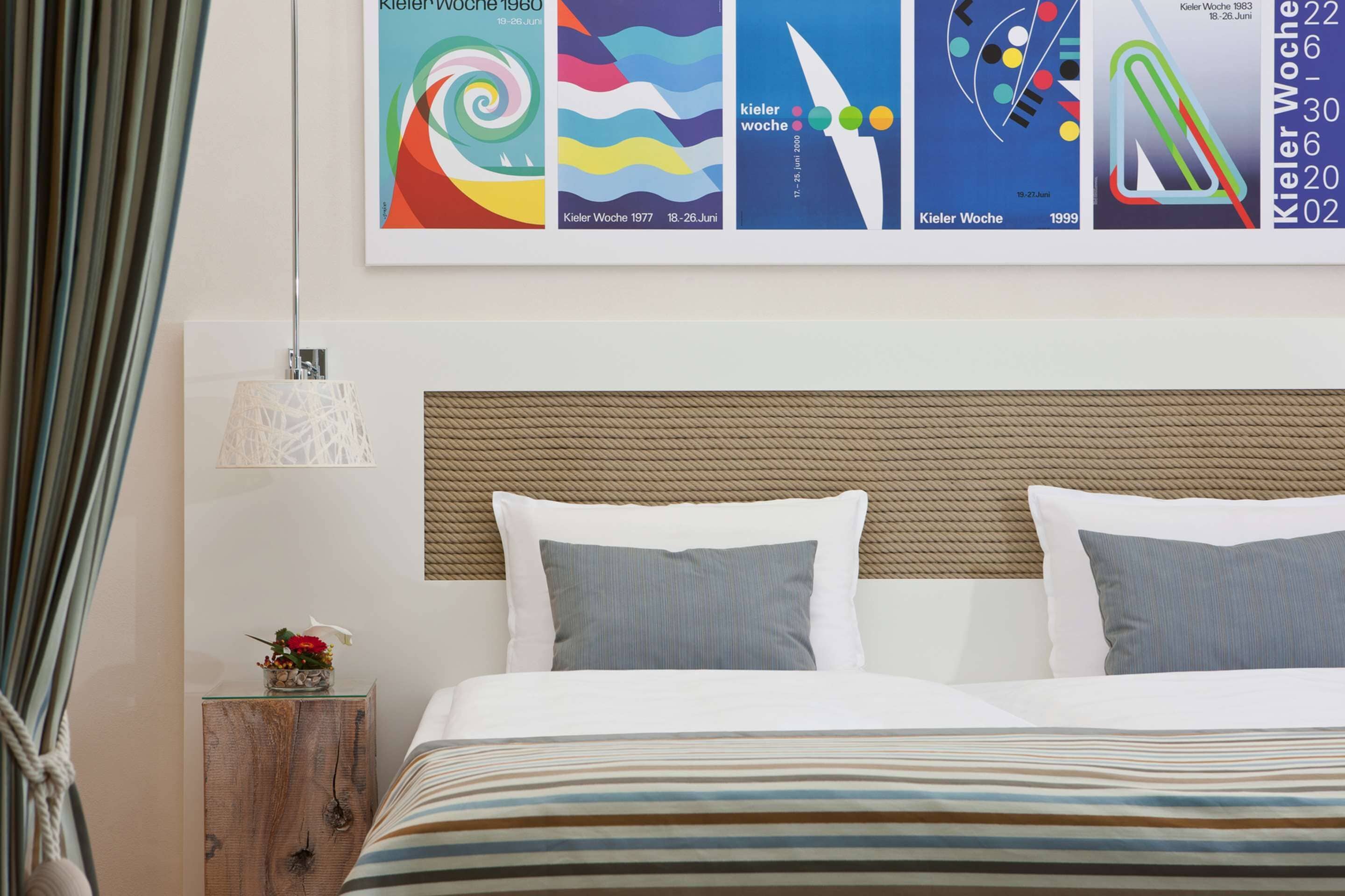 Una camera d'albergo con un letto, cuscini, un comodino, una lampada e una parete decorata con quadri.