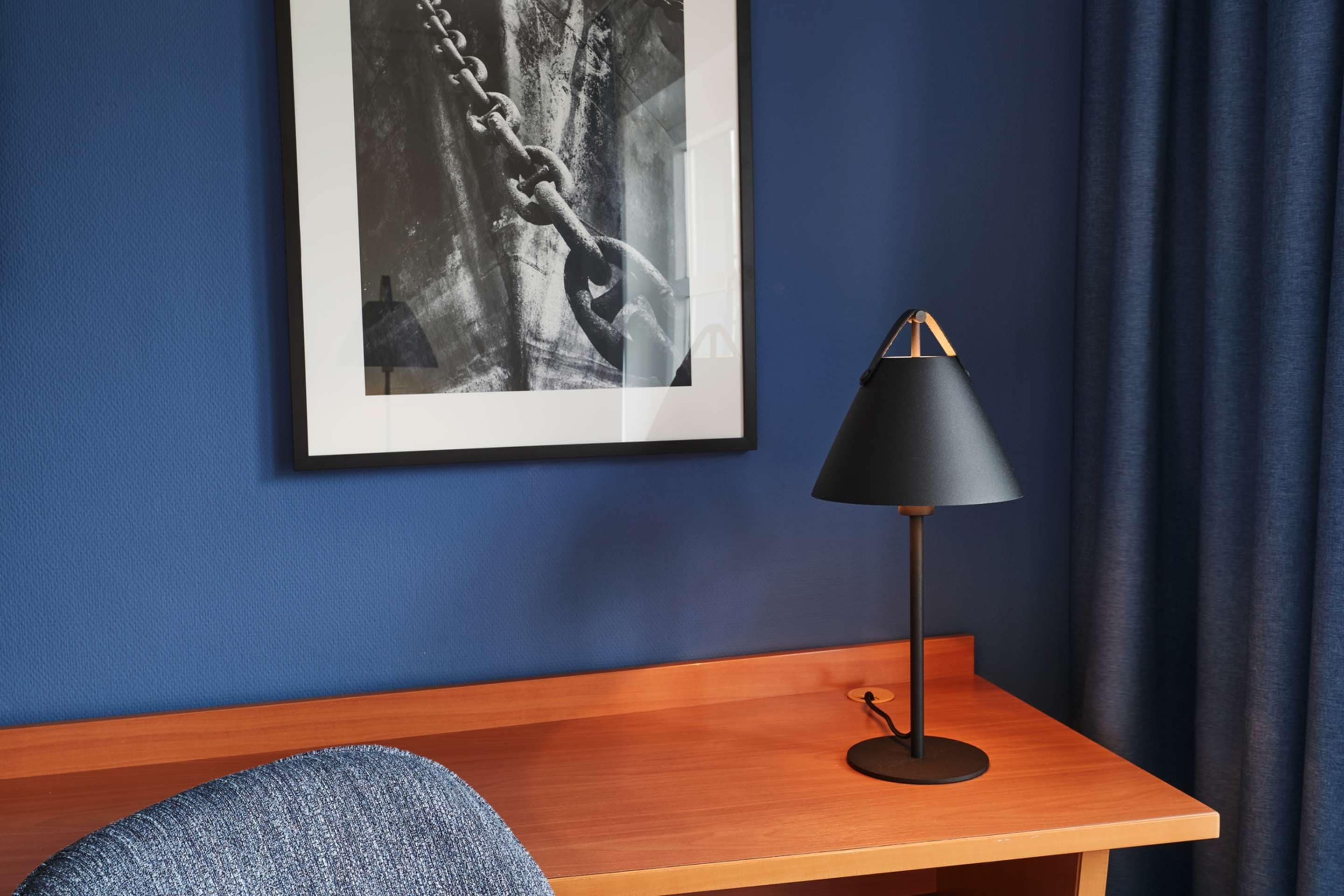 A room with a wooden desk, a black desk lamp, and a framed black and white photograph on the wall.
