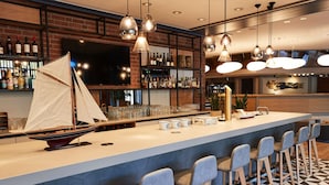 Un área de bar con un modelo de velero, taburetes y una variedad de botellas y copas en estantes.