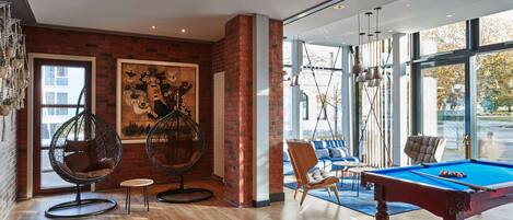 Habitación moderna con mesa de billar, sillas colgantes y un gran ventanal con vistas al exterior.
