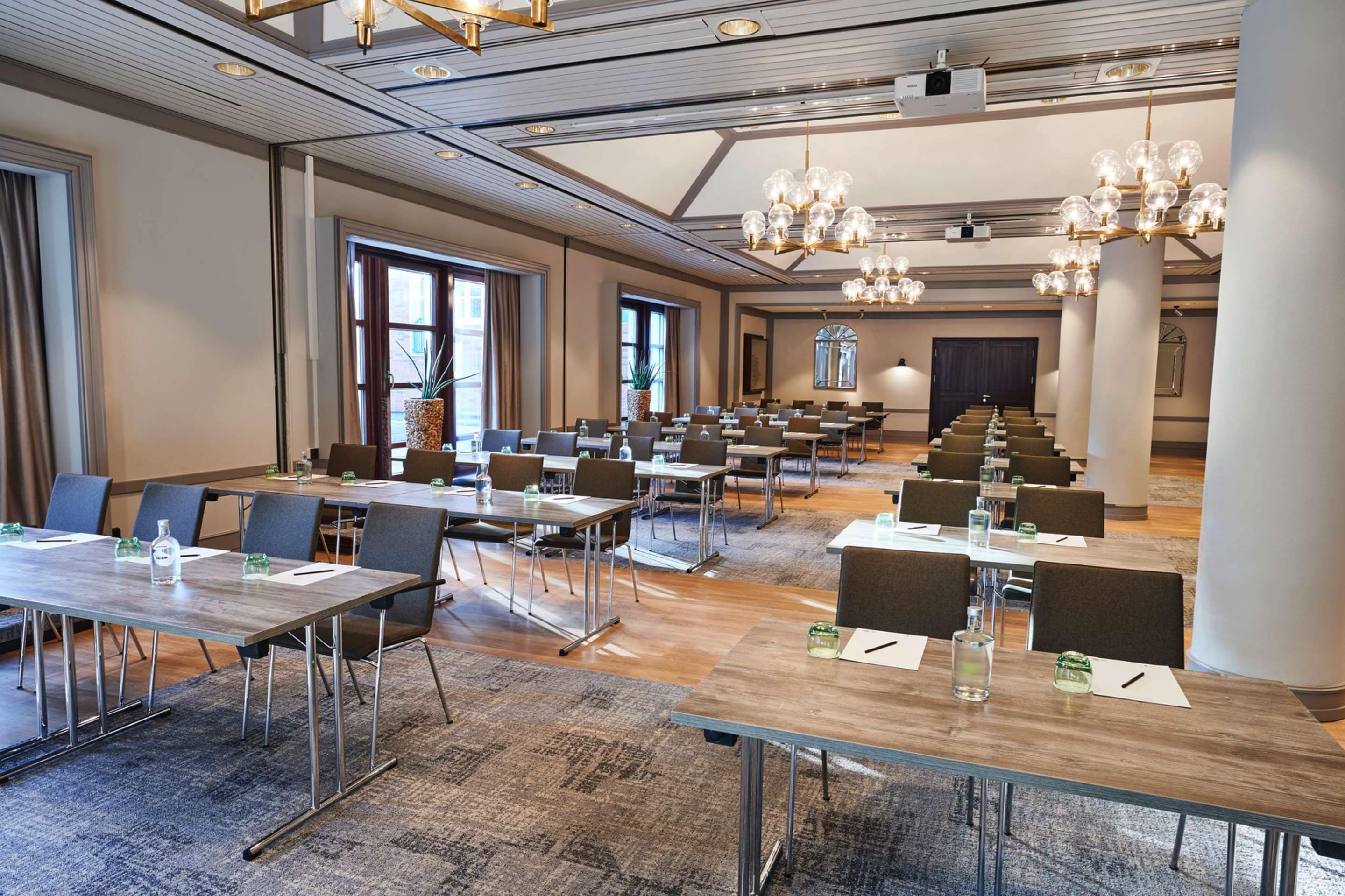 Un salón de conferencias con varias mesas y sillas, ventanas amplias y un candelabro.