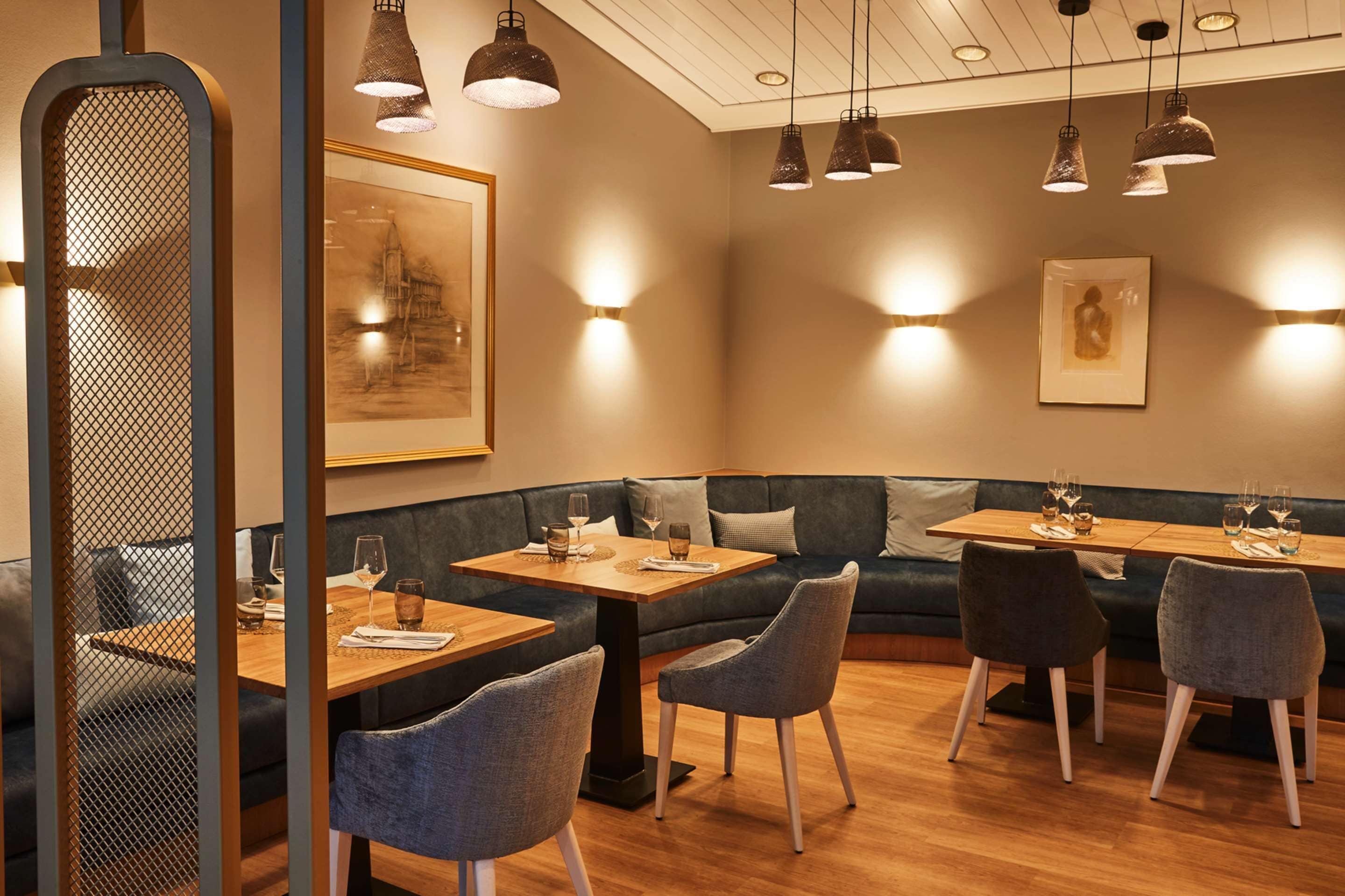 A restaurant interior with wooden tables, cushioned seating, pendant lighting, and artwork on the walls.