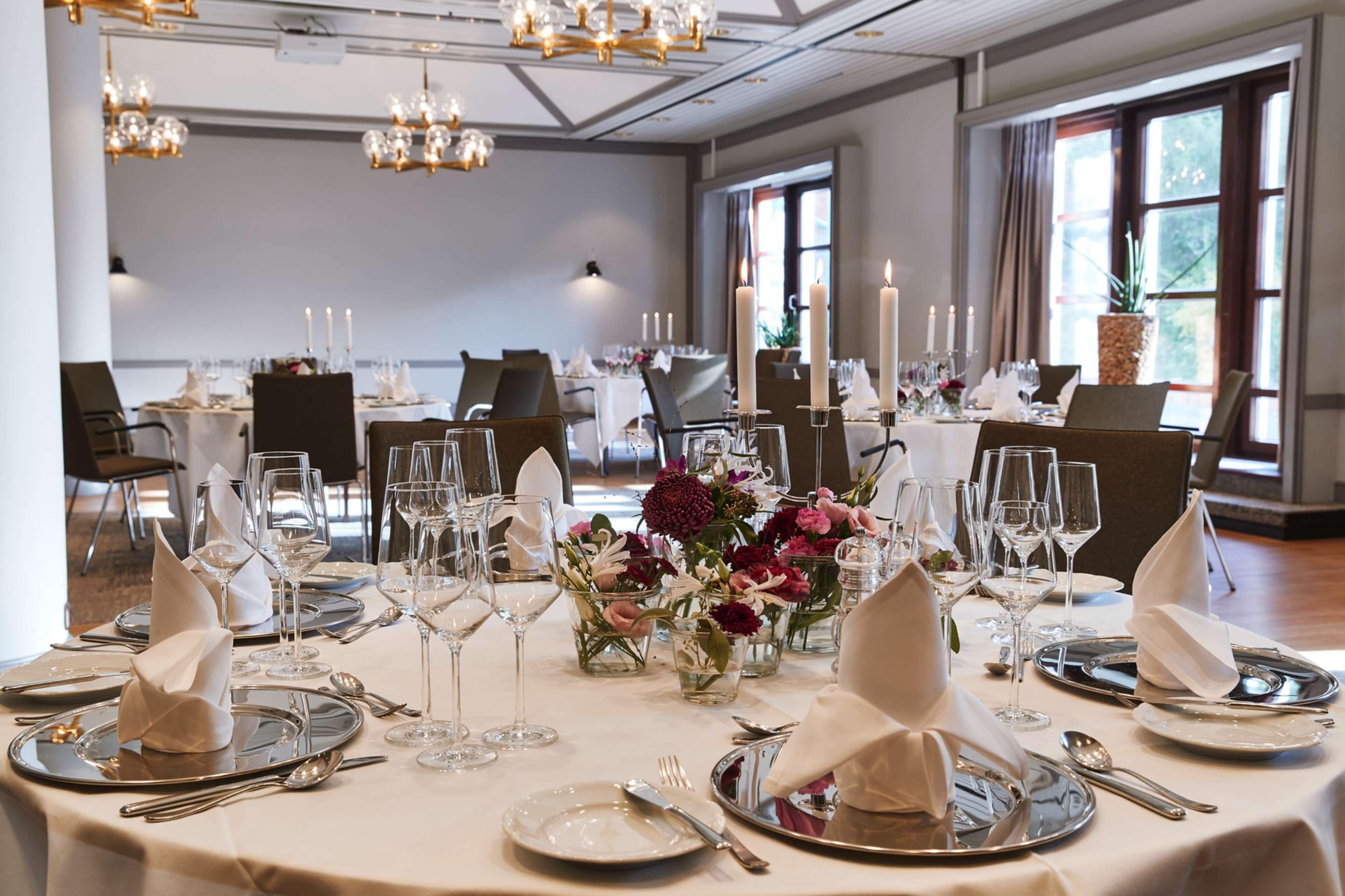 Un salón de banquetes con mesas redondas dispuestas para un evento formal, con manteles blancos, cubertería y centros de mesa con velas.