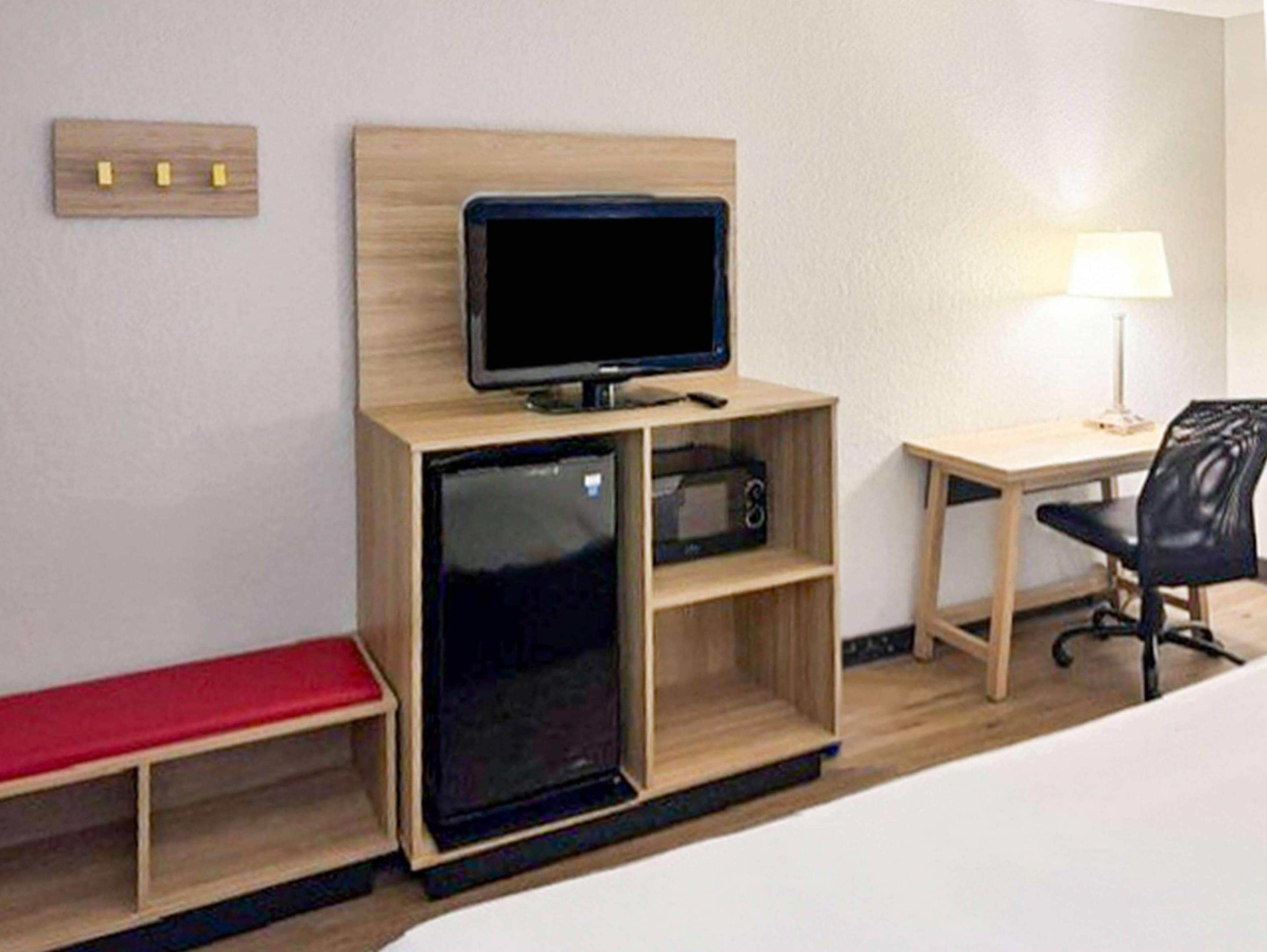 Ein kleines Hotelzimmer mit Bett, Schreibtisch mit Stuhl, kleinem Fernseher, Mikrowelle und einer Bank.
