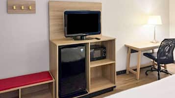 Ein kleines Hotelzimmer mit Bett, Schreibtisch mit Stuhl, kleinem Fernseher, Mikrowelle und einer Bank.